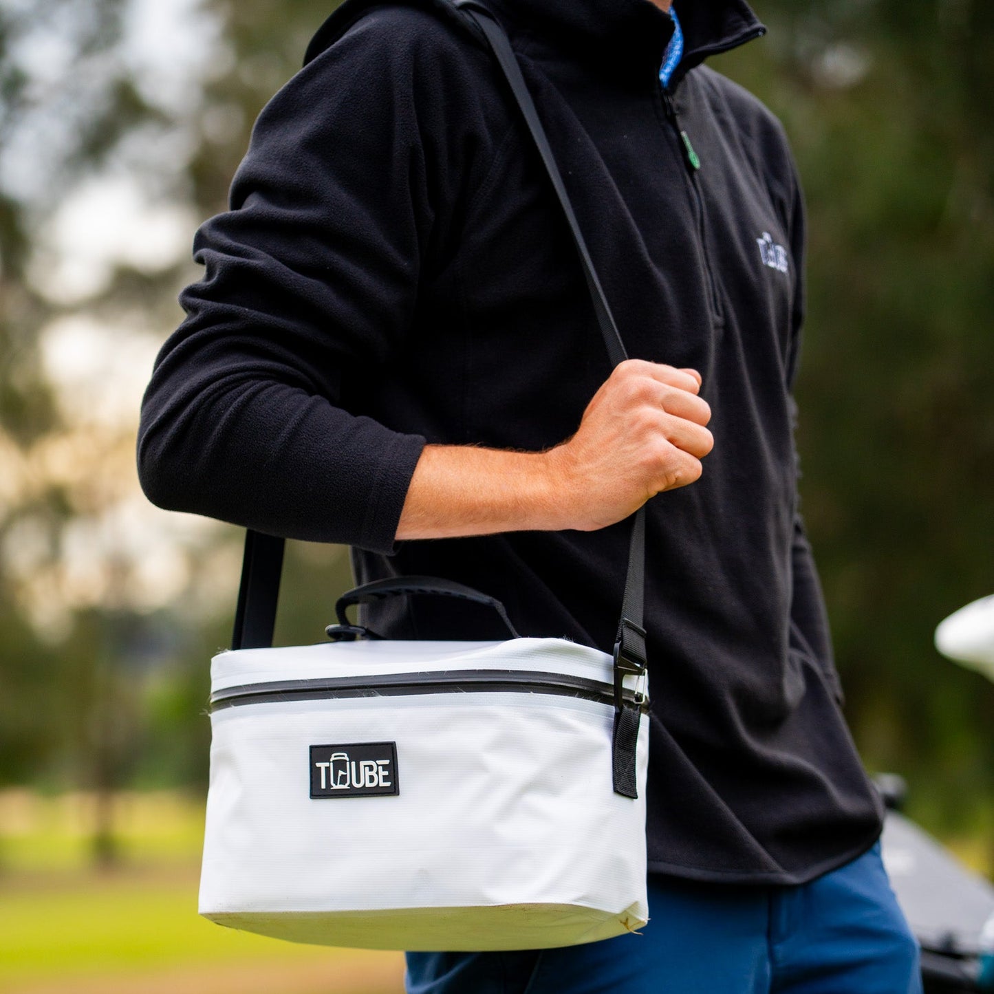 Tuube shoulder strap attached to a Tuube Lunch Box 6L white cooler, hands-free carry demonstrated on course, padded nylon construction