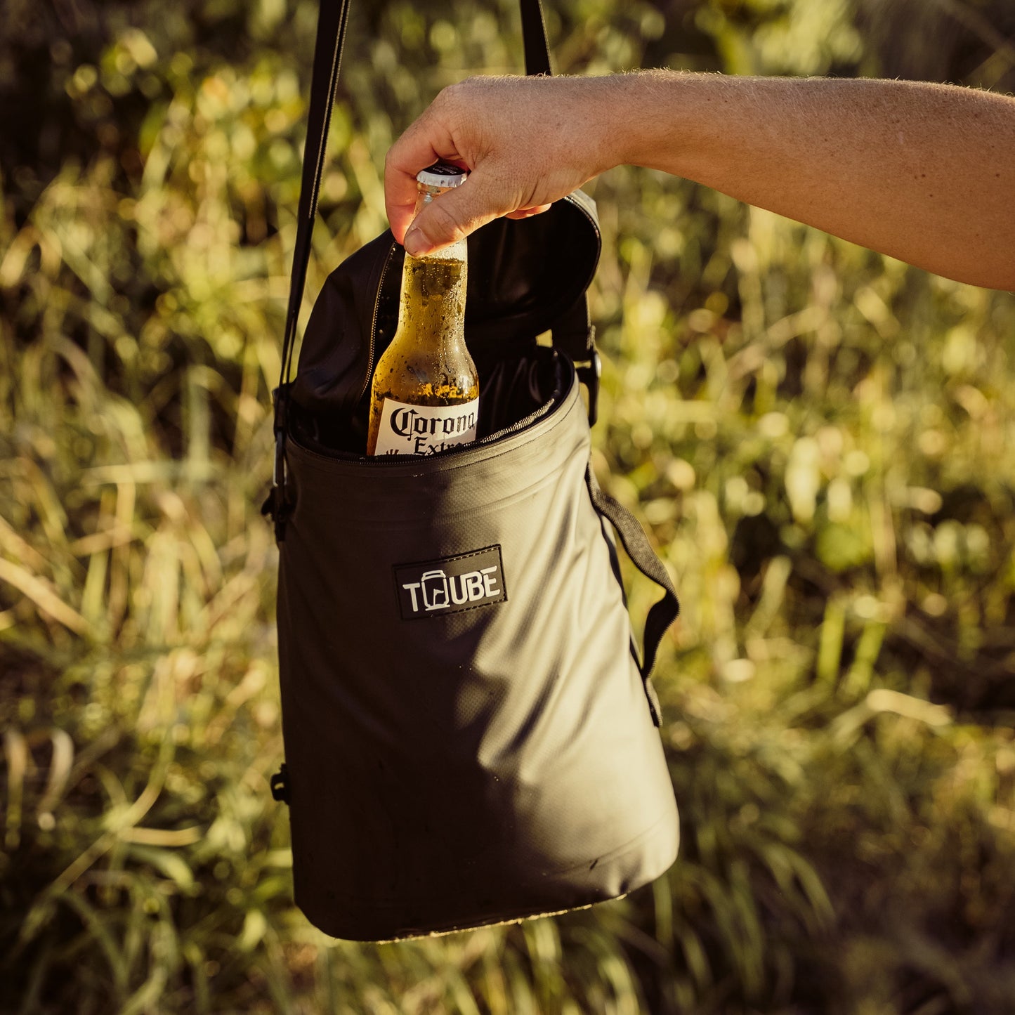 Tuube Weekender 8L black cooler bag carried by handle during a beach trip, leakproof body and heat-welded seams visible on exterior