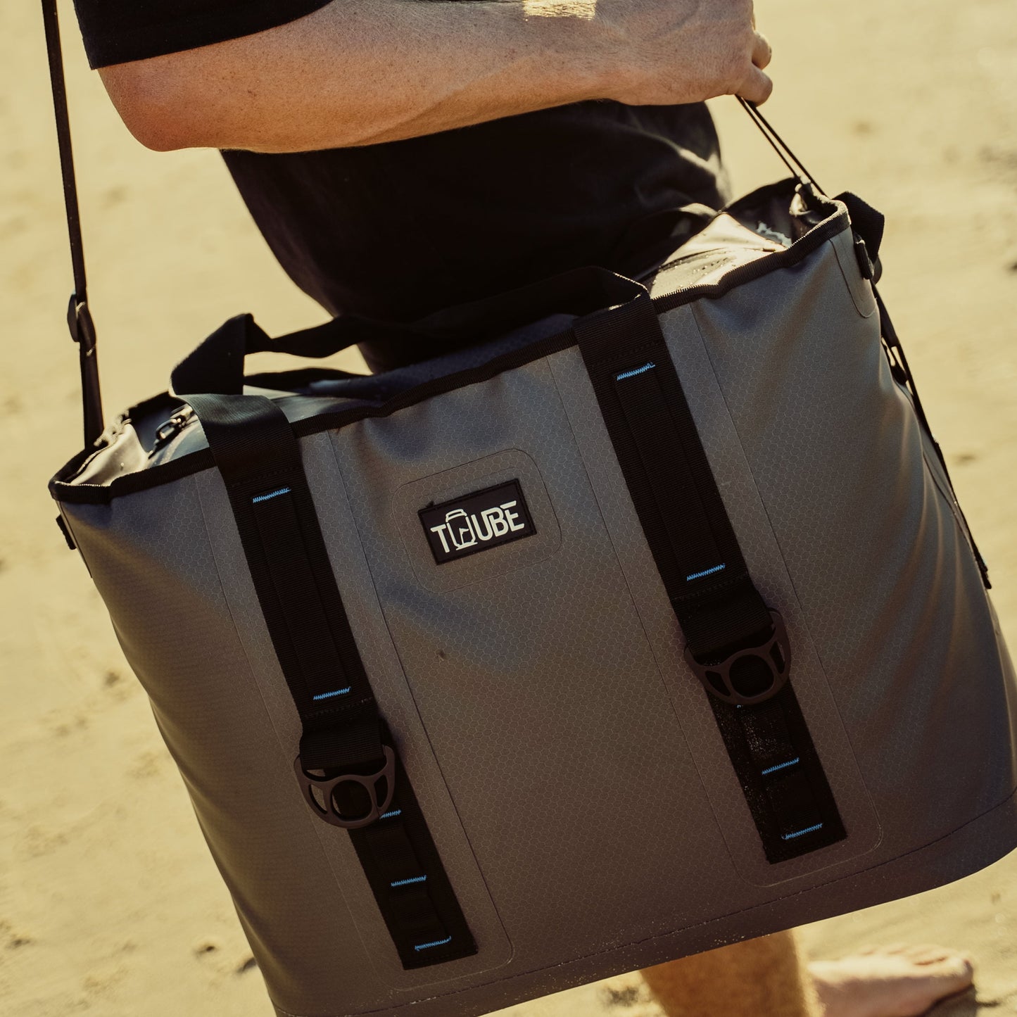 Person carrying Tuube Traveller 36L over one shoulder at dusk, demonstrating adjustable strap comfort for large 36L cooler transport