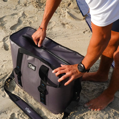 Person opening grey Tuube Traveller 36L cooler bag on a sandy beach, 100% leakproof body and zipper with EVA 25mm insulation