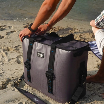 Person holding Tuube Traveller 36L with black straps on a sandy beach, demonstrating shoulder carry comfort for large travel cooler