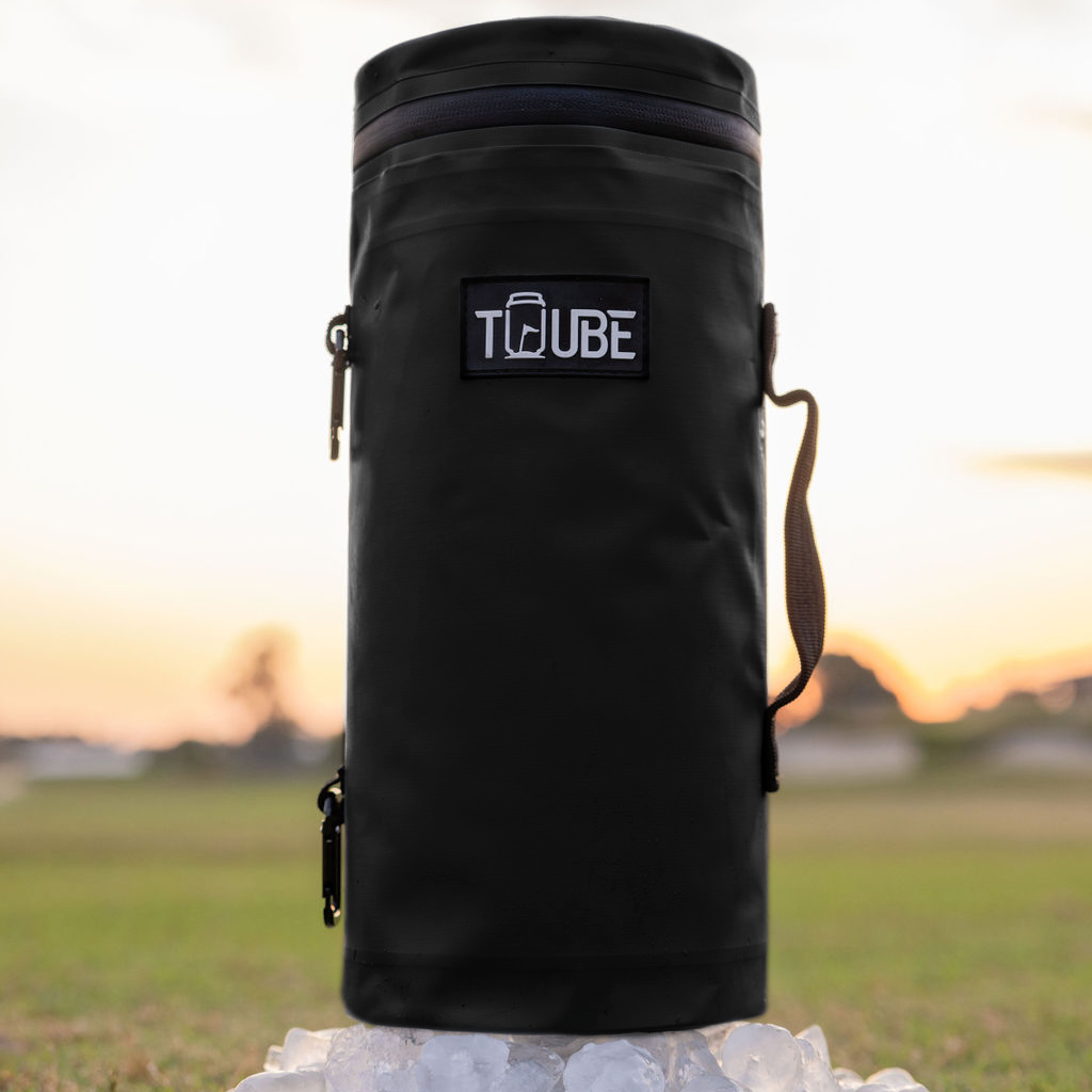 Black Tuube 2.0 cooler bag laid flat on grass showing underside attachment system and heat-welded leakproof seams
