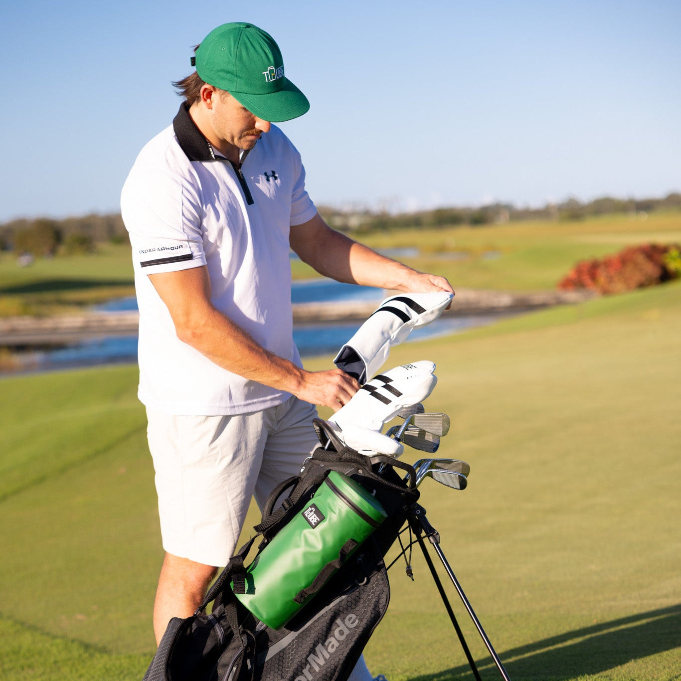 Green Tuube Cooler Bag 2.0 alongside Tuube head covers on a golf course, showing coordinated Tuube golf accessory styling