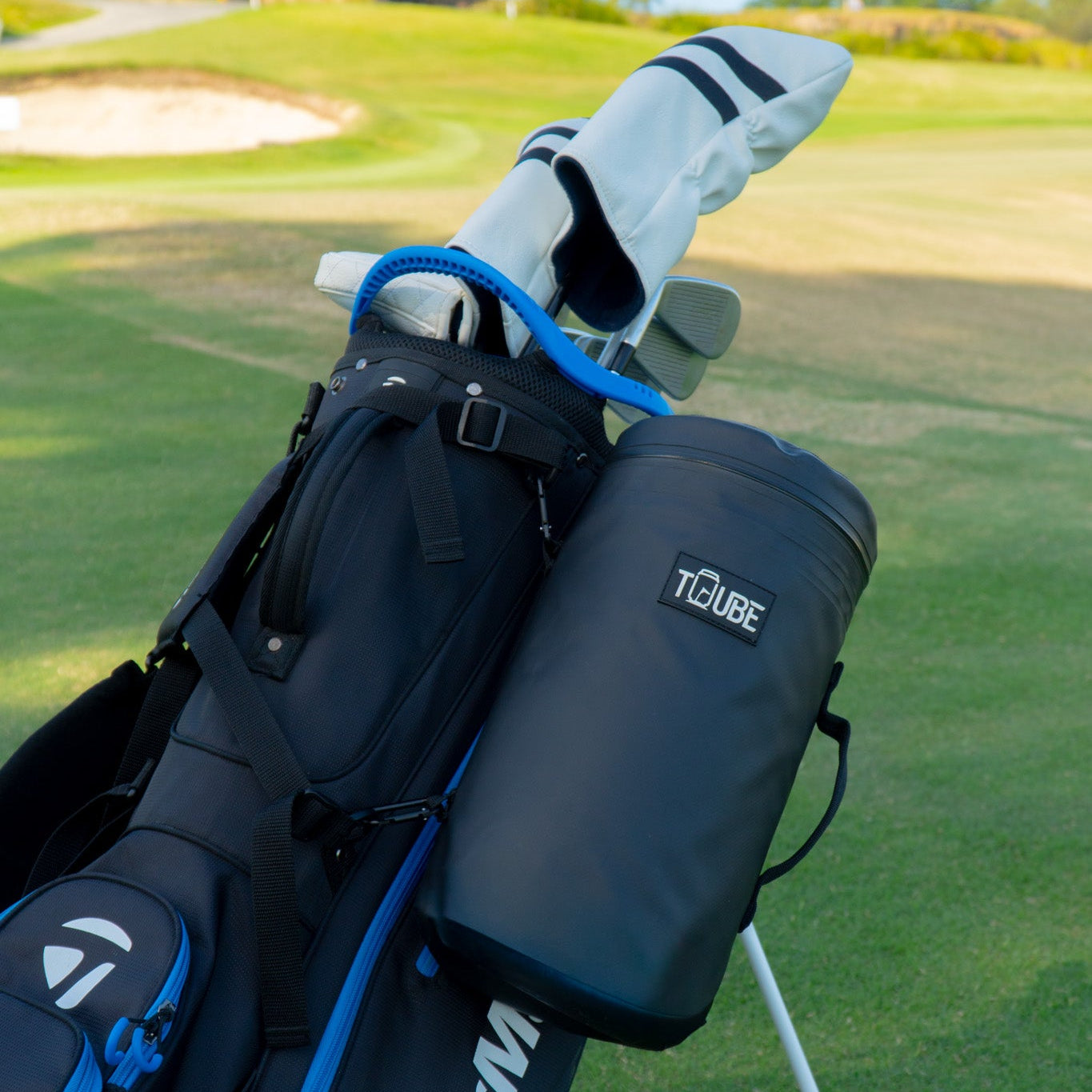 Black Tuube XL cooler bag attached to a golf bag on course, demonstrating dual carabiner clip system for secure attachment