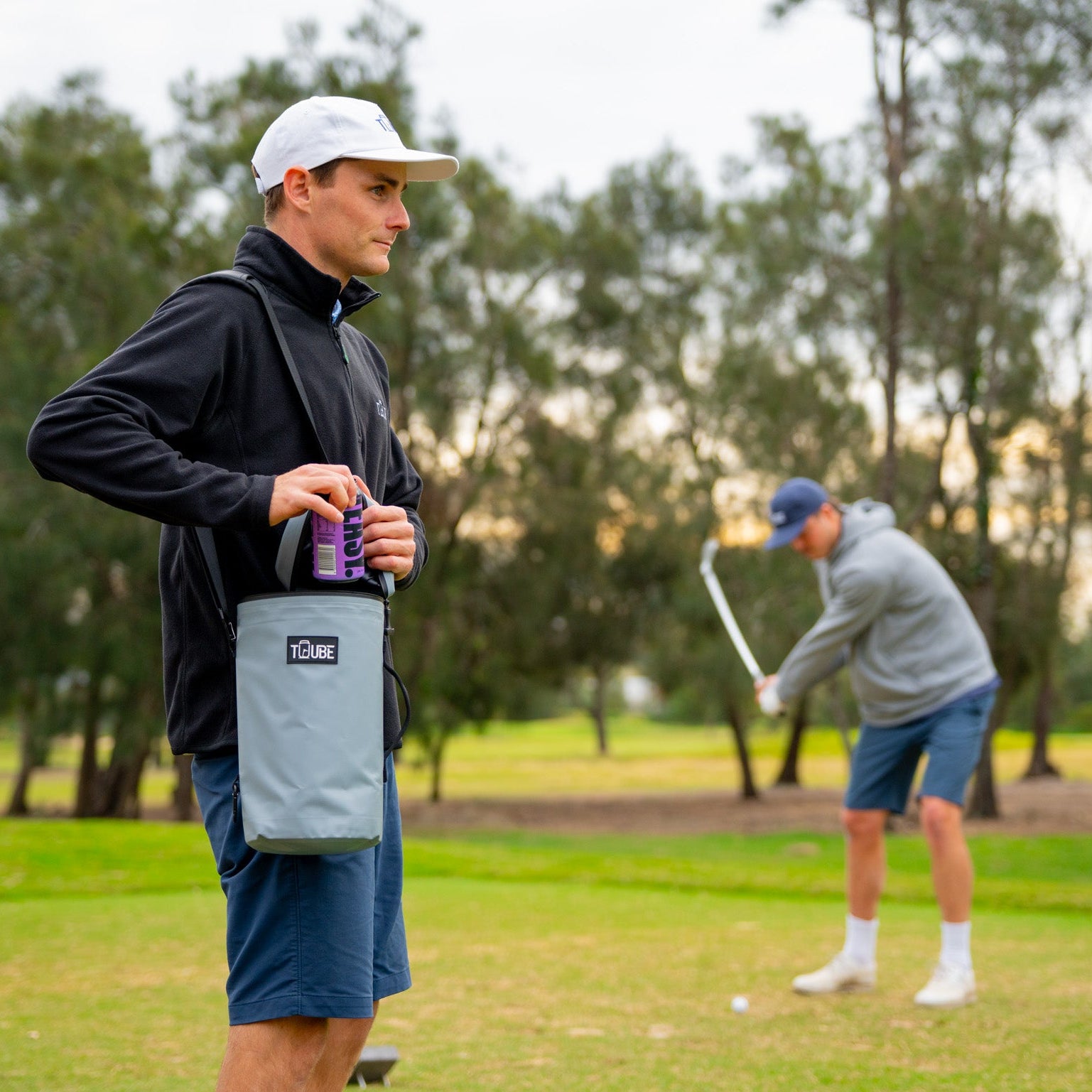 Grey Tuube XL cooler bag clipped to a walking bag on a fairway, 8-can insulated golf cooler in use between holes